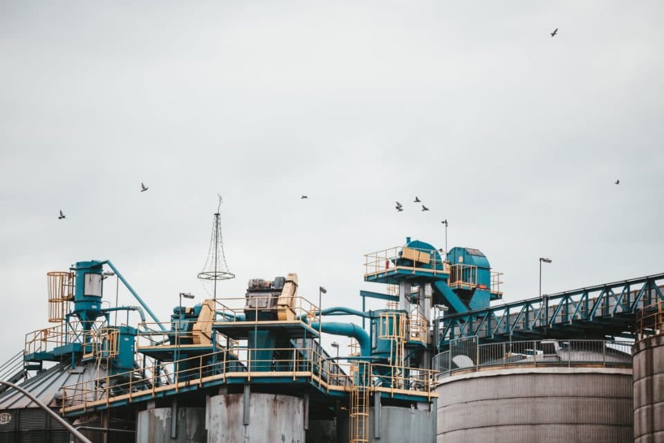 Silos, ciclones e passarelas de uma planta industrial vistos de baixo, sob céu encoberto