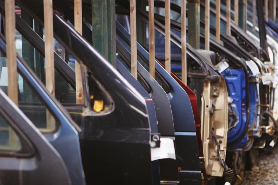 Portas de automóvel penduradas em fila num suporte de linha de montagem, sem ninguém por perto