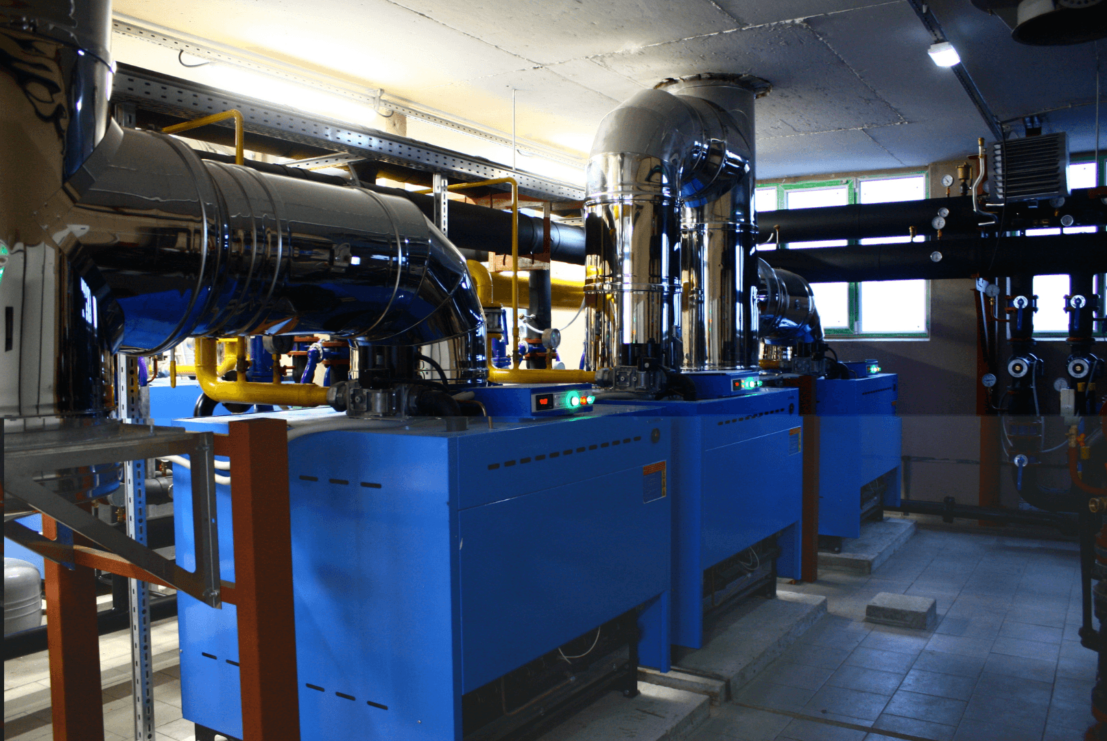 Sala de máquinas com equipamentos azuis, tubulação isolada e dutos de aço inoxidável