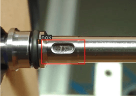 Quadro de um sistema de visão inspecionando uma peça usinada: o achado é cercado e marcado como não conforme.